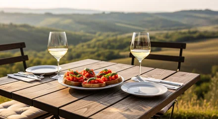 Papier peint photo Toscane A taste of Italy. Fresh bruschetta appetizer and white wine served on a rustic wooden table with a stunning panoramic view of the Tuscan countryside at golden hour.  © Vadym
