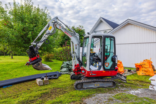 Close up view of Takeuchi TB225 excavator with raised bucket at construction site near white house. Sweden. Stockholm.