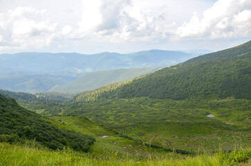 Fototapeta premium Lush green vegetation covers peaceful valley bordered by grassy mountain slopes under cloudy yet bright sky, creating harmonious and tranquil landscape ideal for nature lovers and outdoor enthusiasts