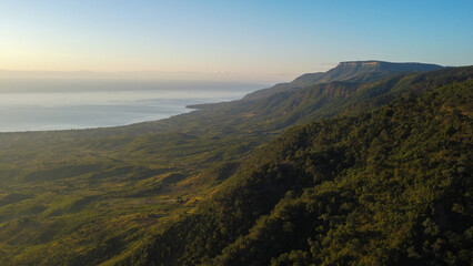 Sweeping vista of verdant hills meeting calm ocean under clear sky, with golden light. malawi