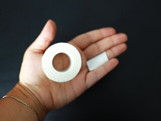 Hand with bandaged finger holding adhesive tape roll on black background