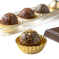 Decadent chocolate truffles adorned with gold accents are displayed in a golden wrapper, complemented by a bar of chocolate, isolated on transparent background