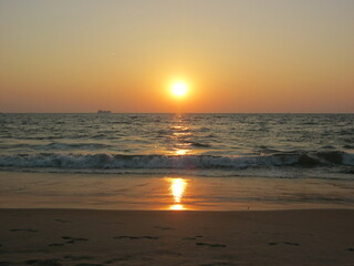 Sunset over calm ocean waves on sandy beach at dusk  