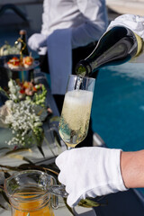 Pouring champagne into glass by waiter in white gloves