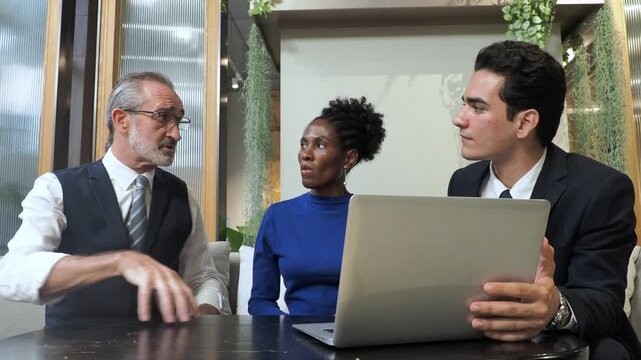 professional engaged in collaborative discussion in modern office. present idea use laptop while other active participate with gesture, seated comfortably around small table and contemporary decor