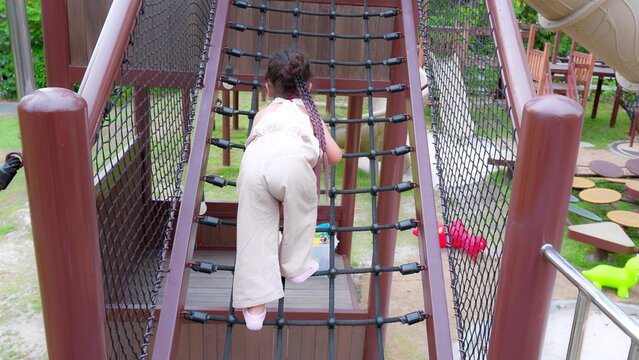 Happy Young Asian child girl climbing a rope bridge at a playground, showcasing outdoor play and adventure.