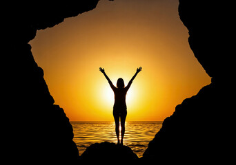 Silhouette of a woman with raised arms between rocks at sunset, symbolizing freedom, success, and a profound sense of personal triumph