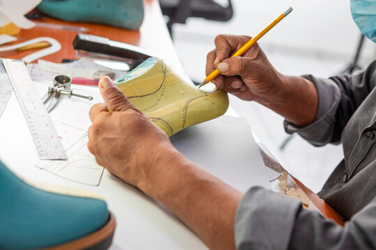 Artisan shoemaker drawing patterns on a shoe last with a pencil, traditional footwear design process, craftsmanship and handmade shoe creation.