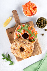 Bagel with salmon, cream cheese, cucumber and arugula on white background. Top view. Copy space