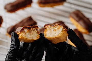 Close up of chocolate eclair with creamy filling held in gloved hands on cooling rack