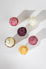 Assorted colorful soft serve ice cream in paper cups on white background, top view