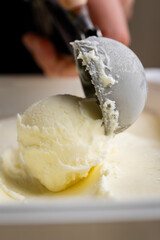 Vanilla ice cream scoop in metal spoon over creamy background, macro food texture shot