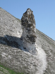 Unique rock formation standing on grassy hill under clear blue sky  