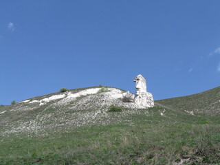 White rock formation on grassy hill under blue sky  