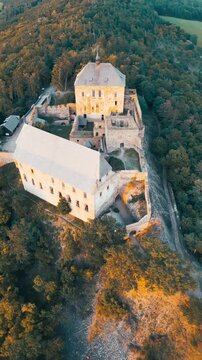 Experience the stunning views as the sun sets behind Tocnik Castle. This medieval ruin stands tall on a hill, surrounded by beautiful landscapes during a summer evening.