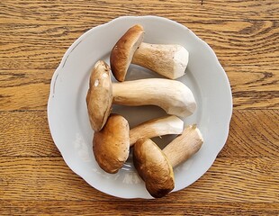 Vier Steinpilze auf einem alten, wei&szlig;en Porzellanteller, Eichenholztisch