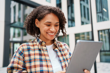 A Smiling Woman Happily Using a Tablet Outdoors in a Modern Urban Setting Surrounded by Nature