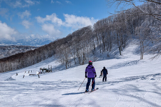Sunny winter landscape with skiers on a snowy mountain slope with trees and blue sky