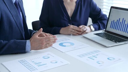 Business colleagues discussing financial data on a laptop and printed documents, analyzing charts and market trends for decisions. Business people and finance concept - Powered by Adobe