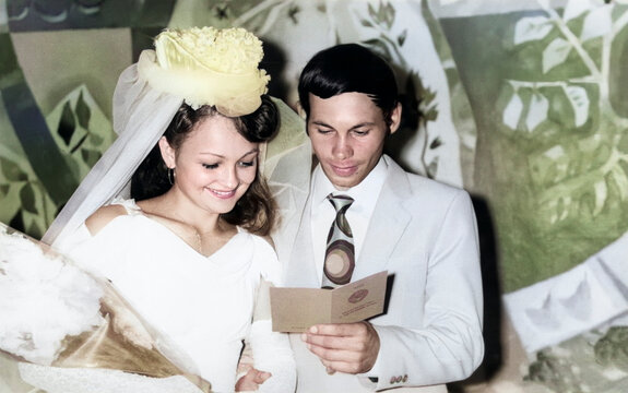 Kharkov, Ukrainian SSR, USSR - July 13, 1981: Vintage portrait of a bride and groom reading a marriage certificate. Retro photo