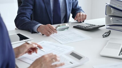 Male financial analysts examining documents, using magnifying glass and calculator while studying corporate data at workplace with a female colleague. Audit and taxes concept - Powered by Adobe