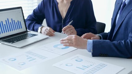Business colleagues discussing financial data on a laptop and printed documents, analyzing charts and market trends for decisions. Business people and finance concept - Powered by Adobe