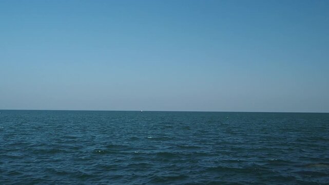 Wide-angle vedeo footage of calm ocean under a clear blue sky, with the horizon line stretching across the frame ideal for sea nature, relaxation, and travel themes and nature lovers.