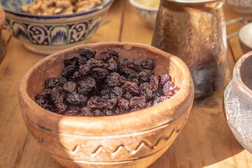A bowl of dark raisins on a wooden table with traditional ceramic dishes and copper jug in the background