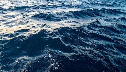 Obraz premium Deep blue water surface, with sun reflecting on the crests and creating light-dark contrasts, textured waves
