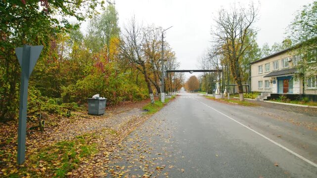 A wide angle shot capturing a quiet, tree lined street in Radianska during autumn. The road stretches into the distance, flanked by vibrant fall foliage in shades of red, orange, and yellow on the lef