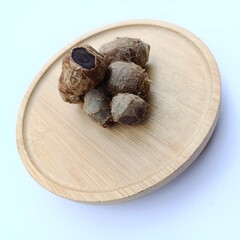 Close-up of fresh black turmeric rhizomes placed on a round wooden plate, showing their unique dark interior, used in traditional medicine and herbal remedies.