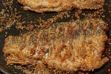 Roast crucian carp. A close-up of an appetizing piece of fish fried until golden crisp in breadcrumbs in a frying pan. A traditional homemade dish made with aromatic spices and oil.