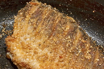 Roast crucian carp. A close-up of an appetizing piece of fish fried until golden crisp in breadcrumbs in a frying pan. A traditional homemade dish made with aromatic spices and oil.