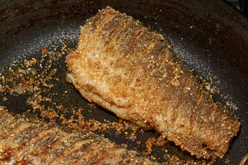 Roast crucian carp. A close-up of an appetizing piece of fish fried until golden crisp in breadcrumbs in a frying pan. A traditional homemade dish made with aromatic spices and oil.