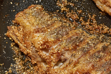 Roast crucian carp. A close-up of an appetizing piece of fish fried until golden crisp in breadcrumbs in a frying pan. A traditional homemade dish made with aromatic spices and oil.