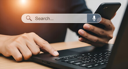 Person using a smartphone and laptop to search online with a search bar and microphone icon overlay