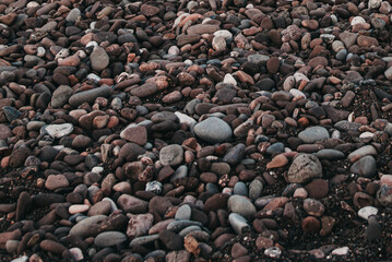 Smooth water-worn river rocks on a beach, natural stone texture background with gray, white, red, brown, and black pebbles, rounded stones polished by water, soft organic surface pattern
