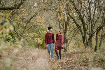 Naklejka premium An authentic, candid scene shows a couple strolling through a sunlit autumn forest, wearing casual fall apparel, capturing a genuine connection amid golden leaves and quiet, natural beauty.