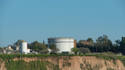 Industrial storage tanks situated on a grassy bluff overlooking an area. Representing energy infrastructure & industrial landscapes