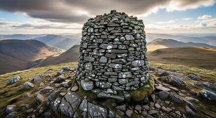 Stone cairn stands as a rugged landmark amidst a mountain range landscape under cloudy sky