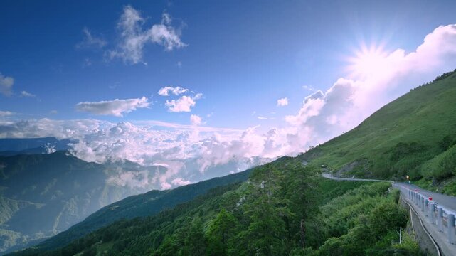 Aerial view of Hehuanshan, Renai, Nantou, Taiwan. Early autumn sun lights a winding mountain road above a sea of clouds and green slopes.