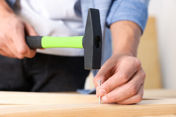 Man hammering nail into wooden plank indoors, closeup