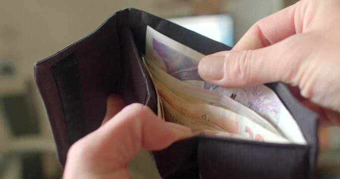 A person examining the cash contained within a black wallet, drawing attention to the different denominations of banknotes and the wallets organized interior layout and design