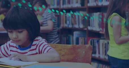 Girl in striped T-shirt reading open book at wooden table in library, with bookshelves, copy space