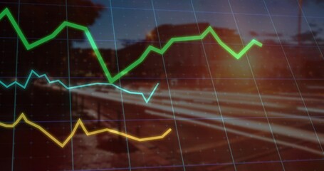 Displaying tri color line graph curves over gridlines, blurred rural railway at dusk with sun flare