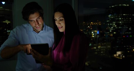 Examining tablet, two business casual colleagues collaborating at office window with city skyline