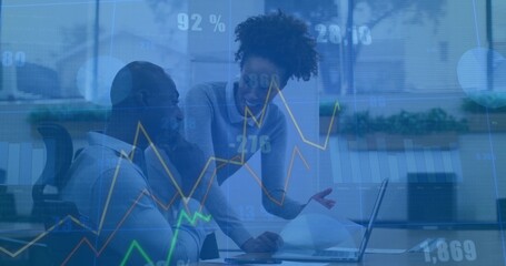 Working colleagues studying laptop and pointing at display at desk with plants, overlaying charts