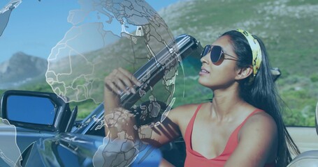Sitting Indian woman sporting sunglasses in convertible, gazing upward on road, with globe overlay