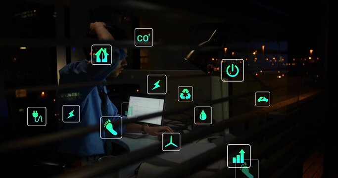 Reviewing engineer in tie monitoring laptop with eco icons at night office view, copy space - Powered by Adobe