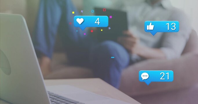 Man holding tablet on sofa in living room, laptop on coffee table, social-media-icons, copy space - Powered by Adobe